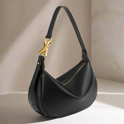 leather shoulder bag in a  half moon shape. It features bold brushed gold cross detailing. Black